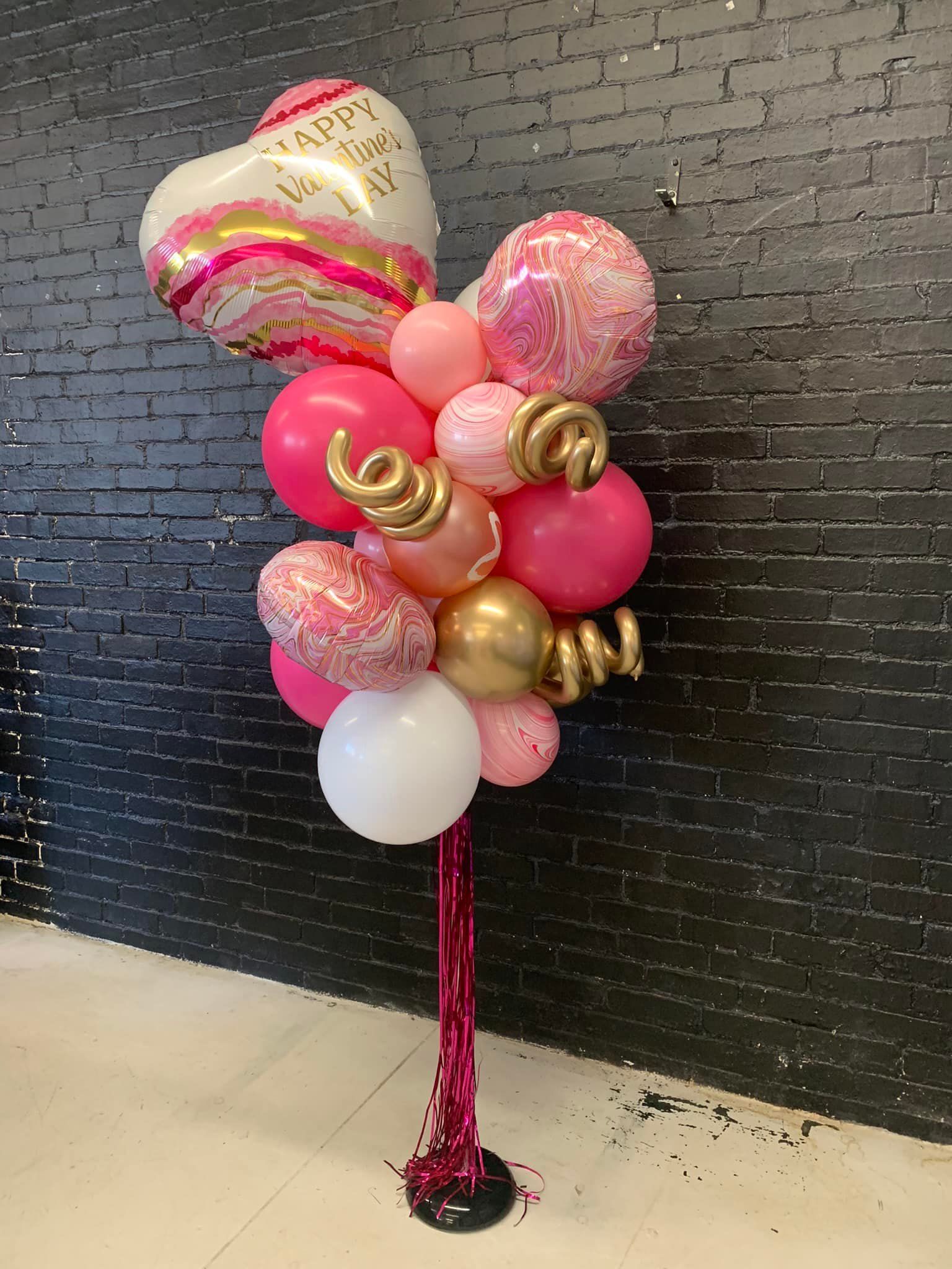 A bunch of pink and gold balloons on a stand in front of a brick wall.