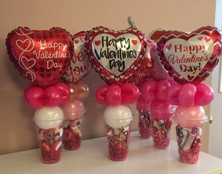 A table topped with cups filled with candy and balloons for valentine 's day.