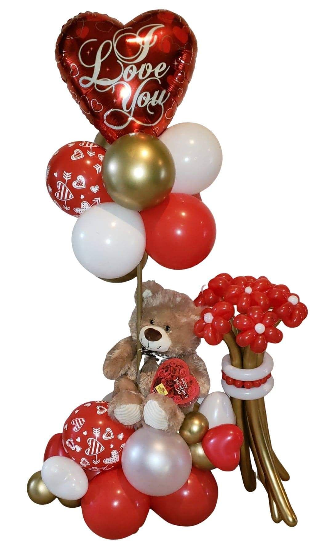 A teddy bear is sitting on top of a bunch of red and white balloons.