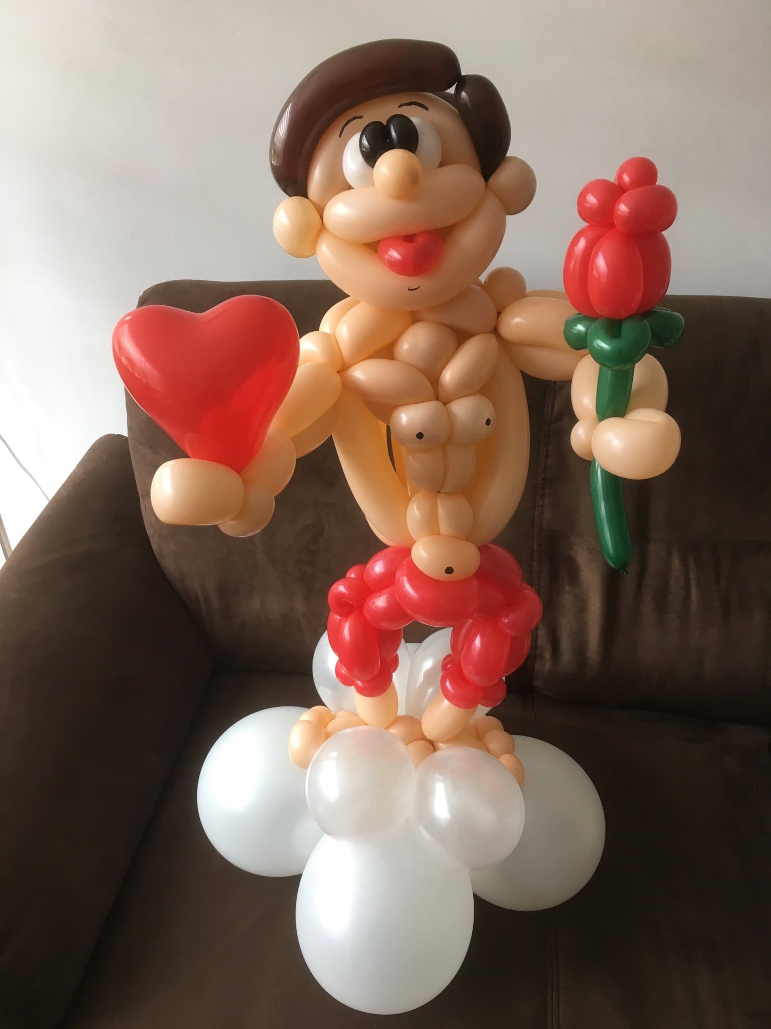 A man made out of balloons is holding a heart and a rose
