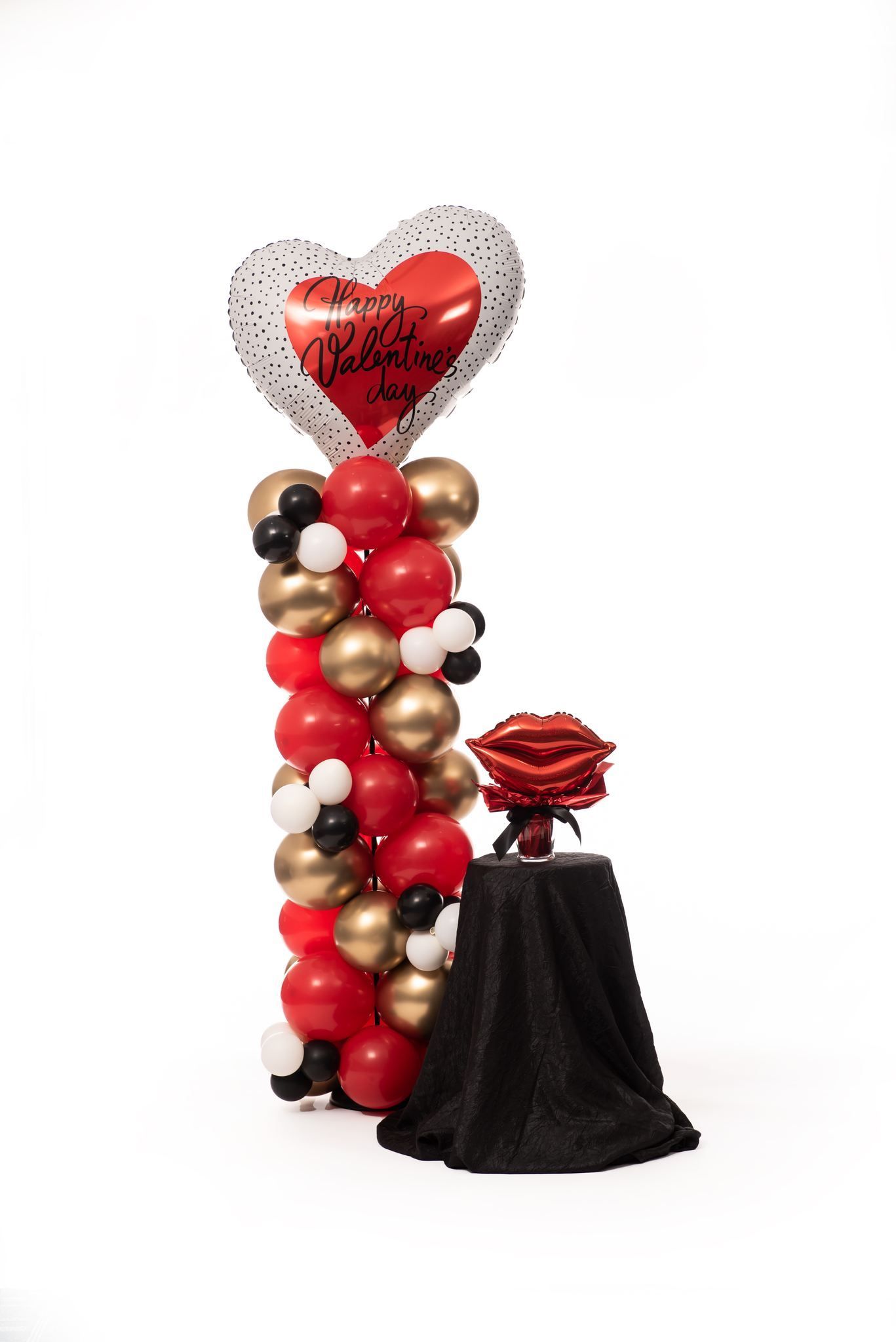 A balloon tower with a heart shaped balloon and a rose on a table.