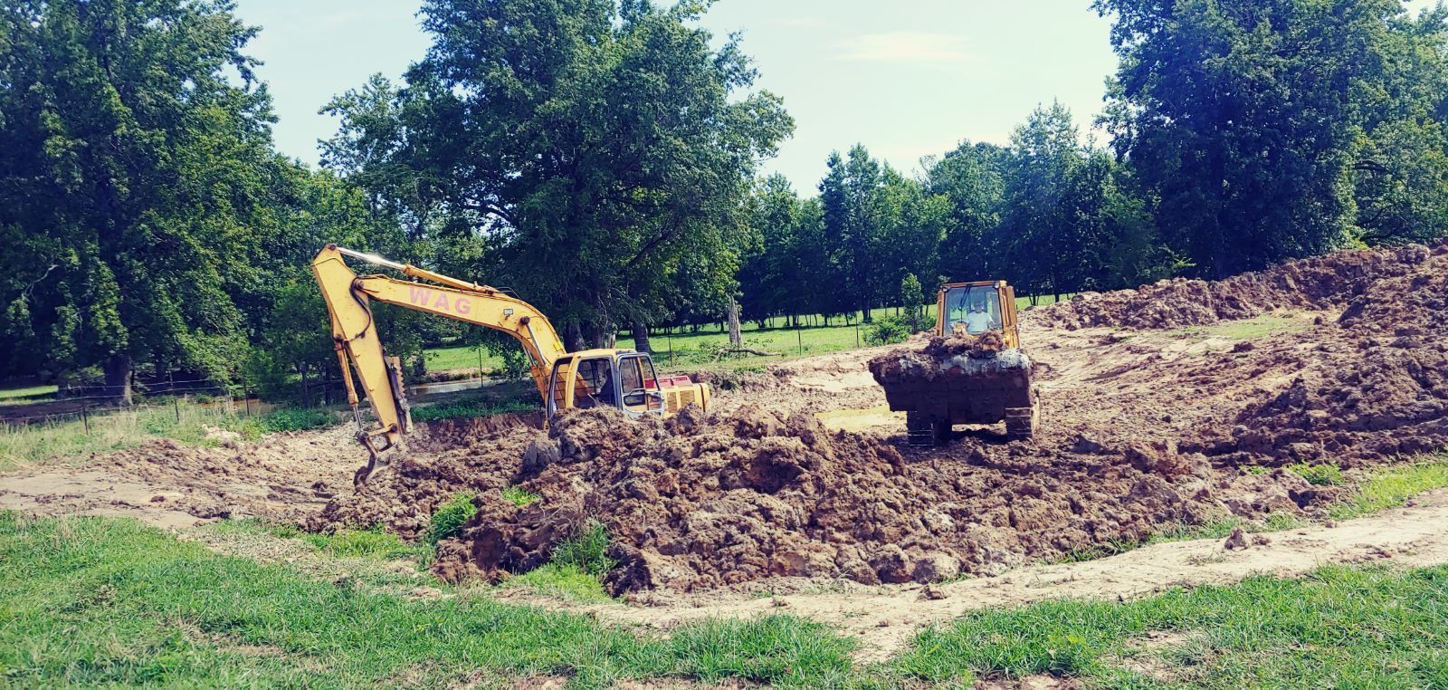 A yellow excavator is digging a hole in a field.
