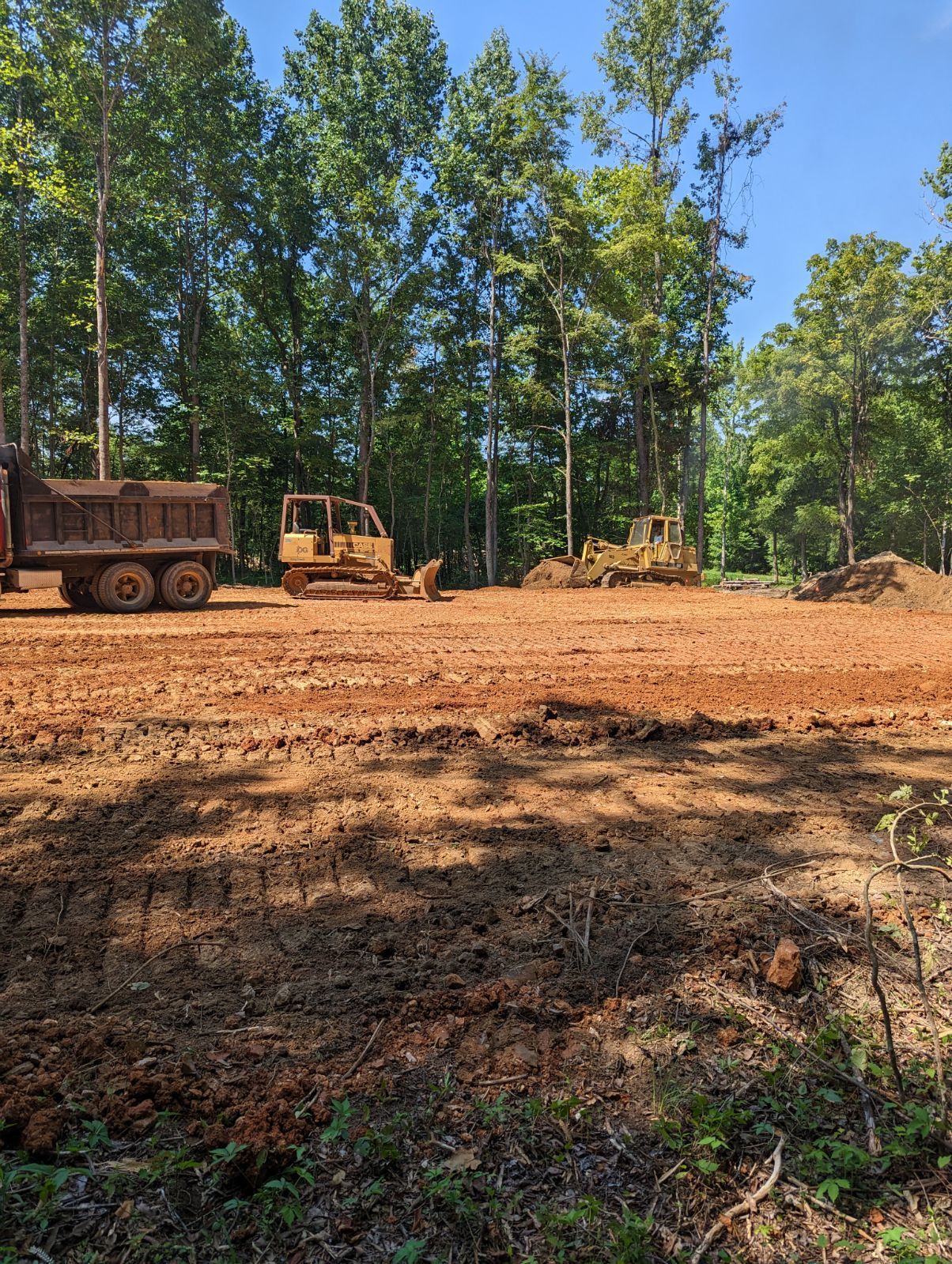 A dump truck is parked in a dirt field next to a bulldozer.