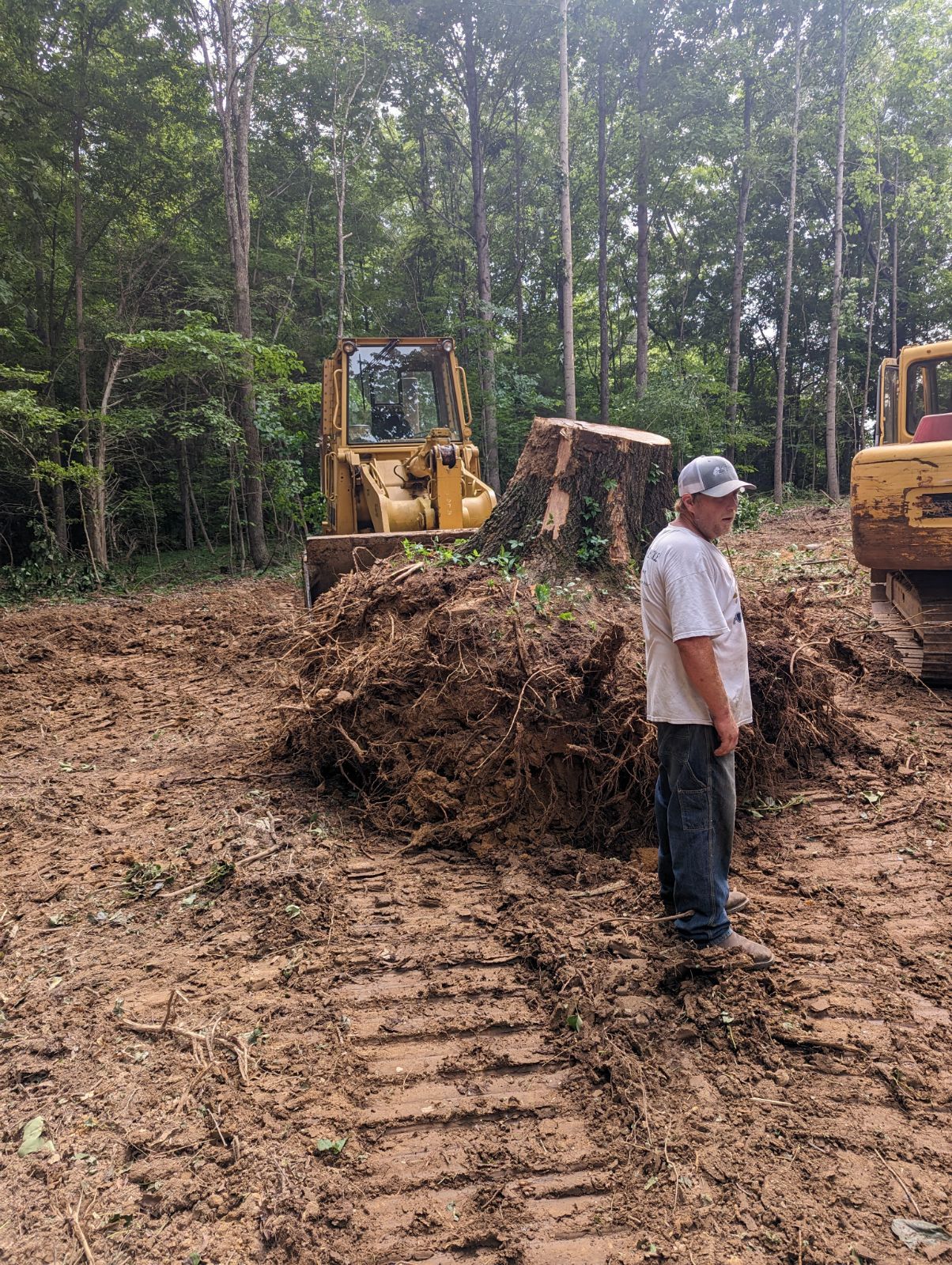 A man is standing in front of a bulldozer in a dirt field.