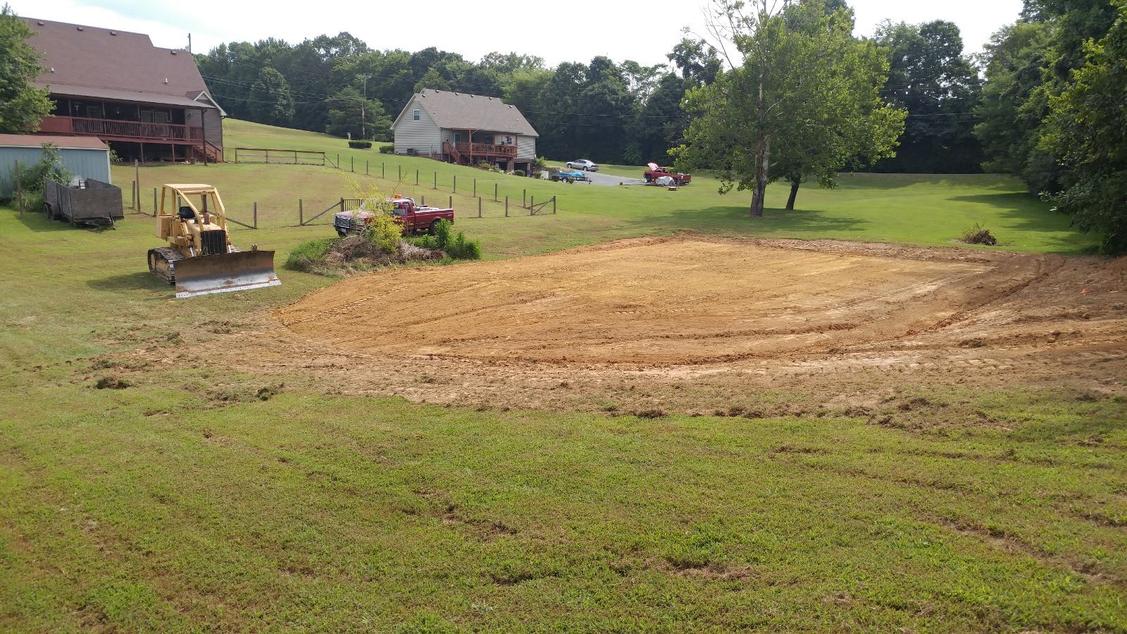 A bulldozer is working on a dirt field in front of a house.