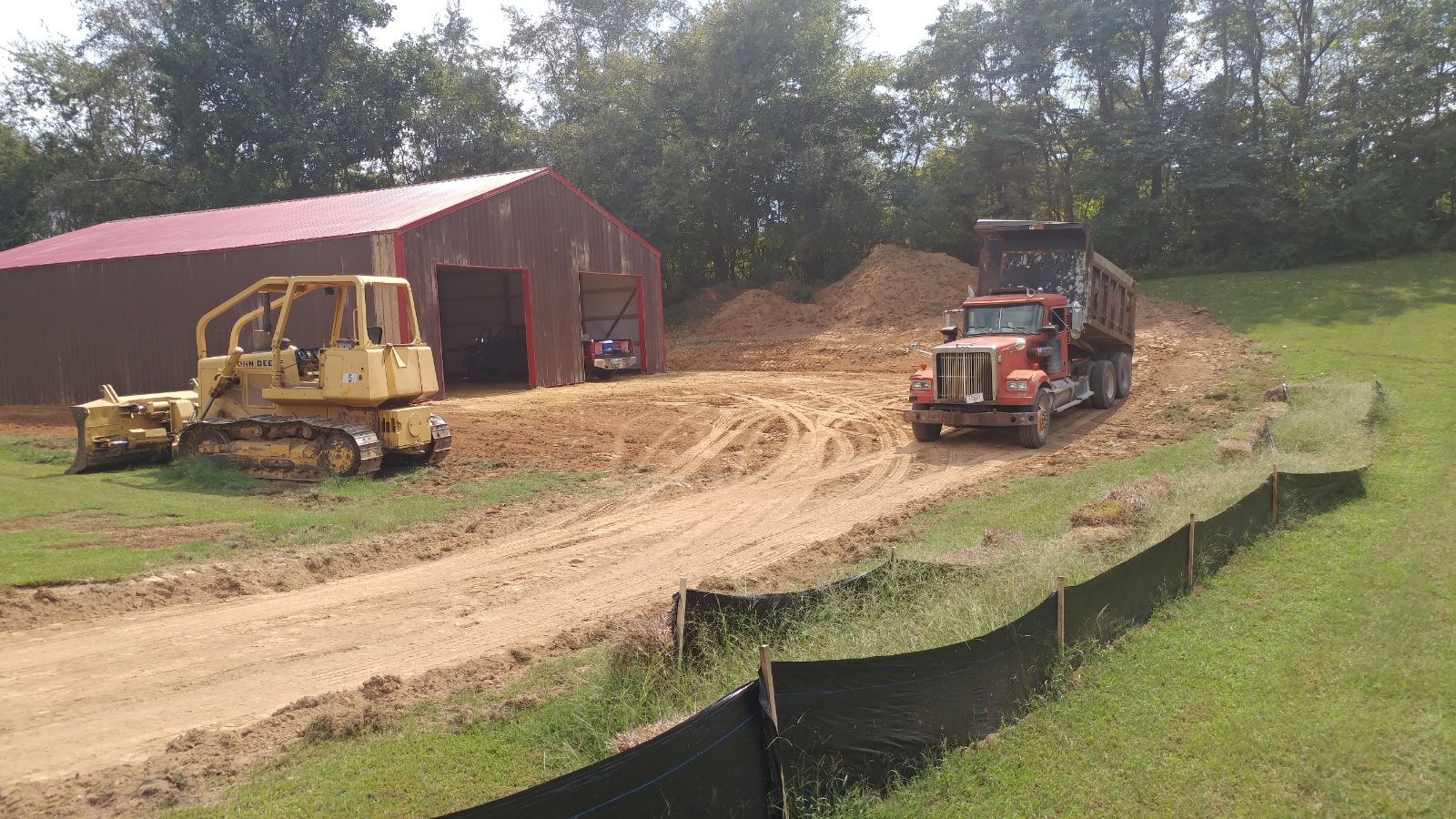 A bulldozer and a dump truck are driving down a dirt road.