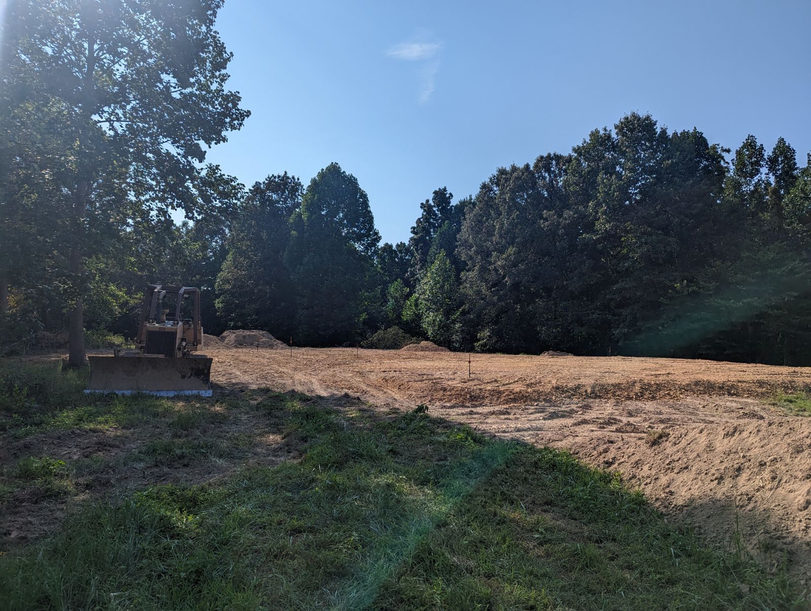A bulldozer is in the middle of a field with trees in the background.