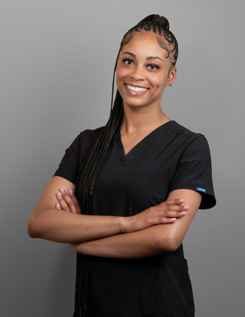 A woman in a black scrub top is smiling with her arms crossed