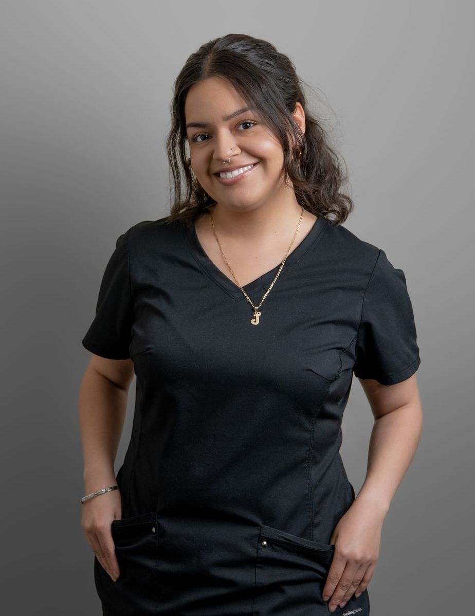 A woman in a black scrub top is smiling and holding her hands in her pockets.