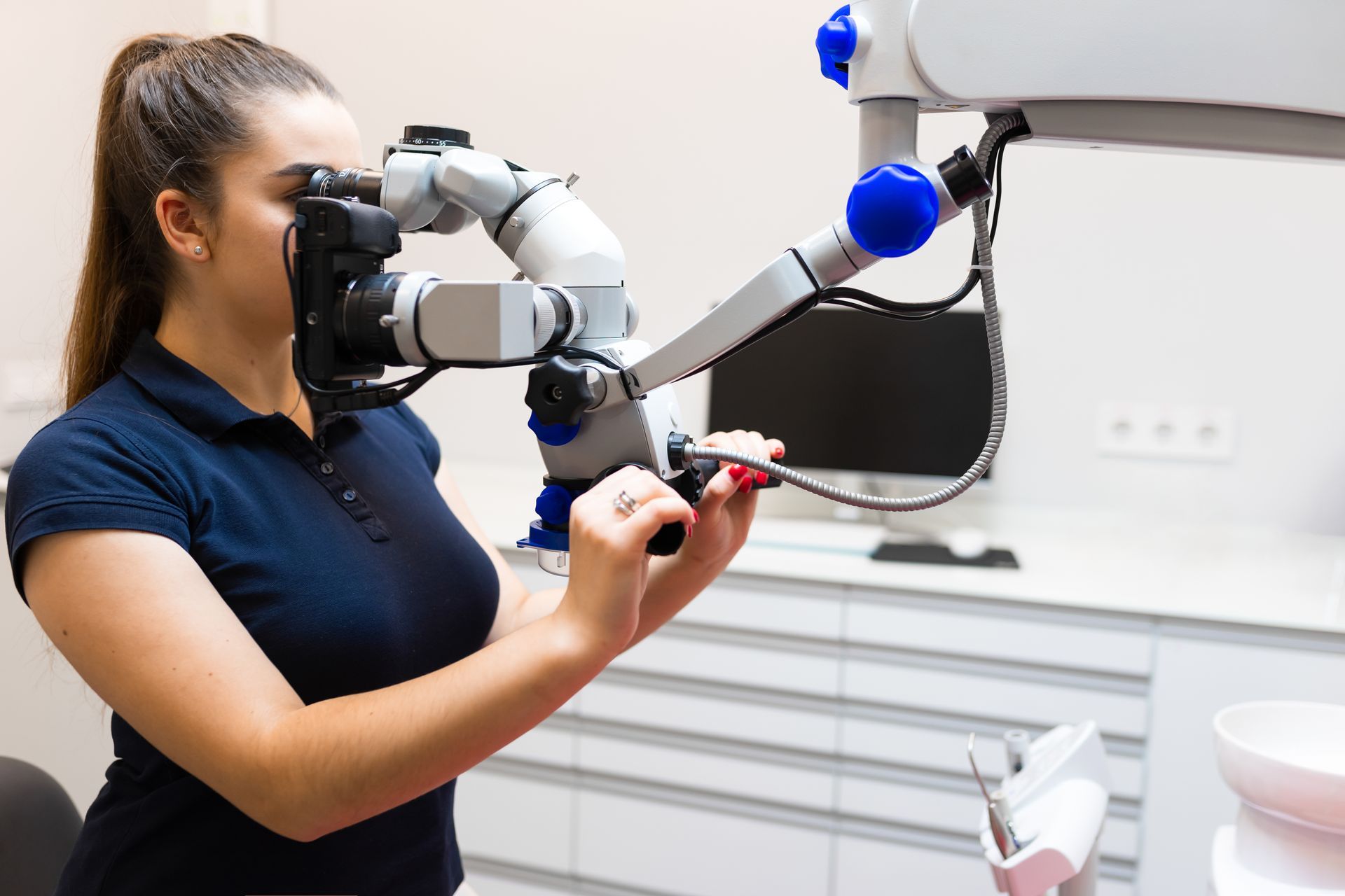 A woman is using a dental microscope in a dental office.