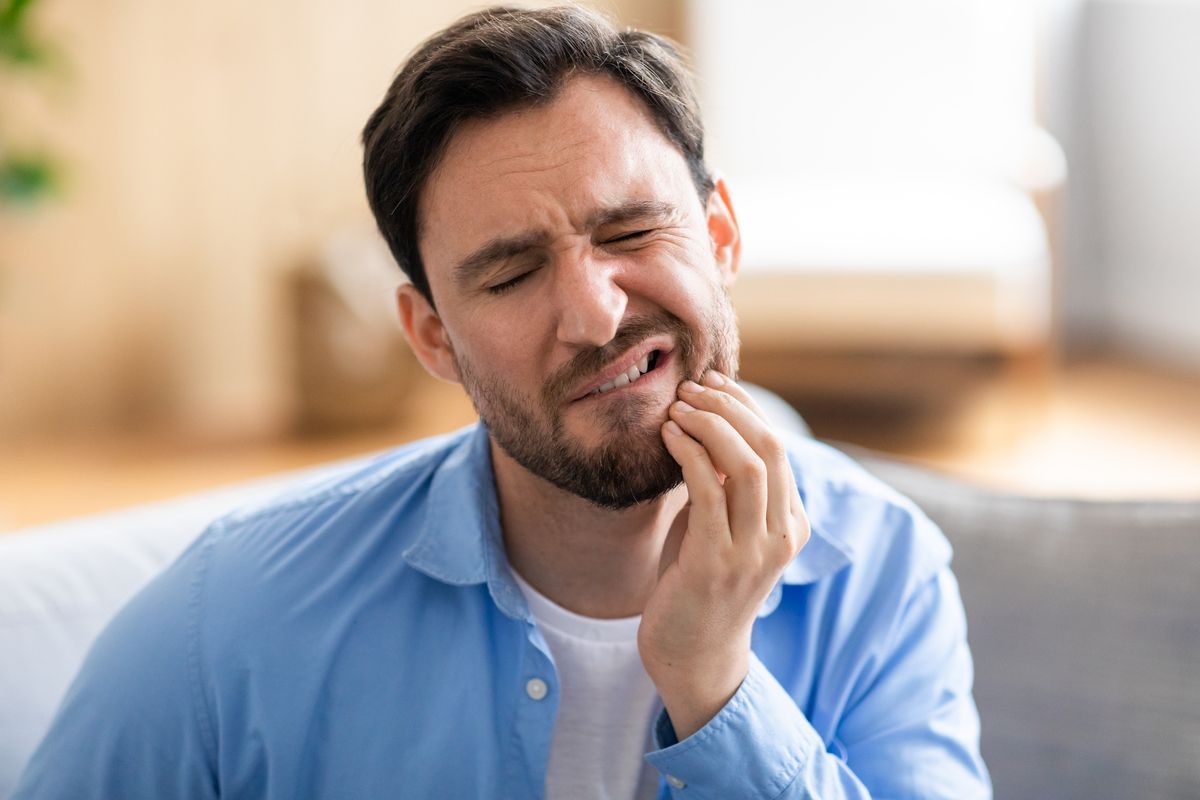Man clutching his jaw in pain on a sofa, wearing a blue shirt
