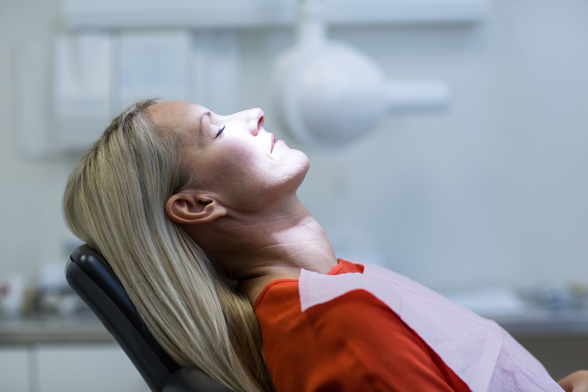 A woman is laying in a dental chair with her eyes closed.