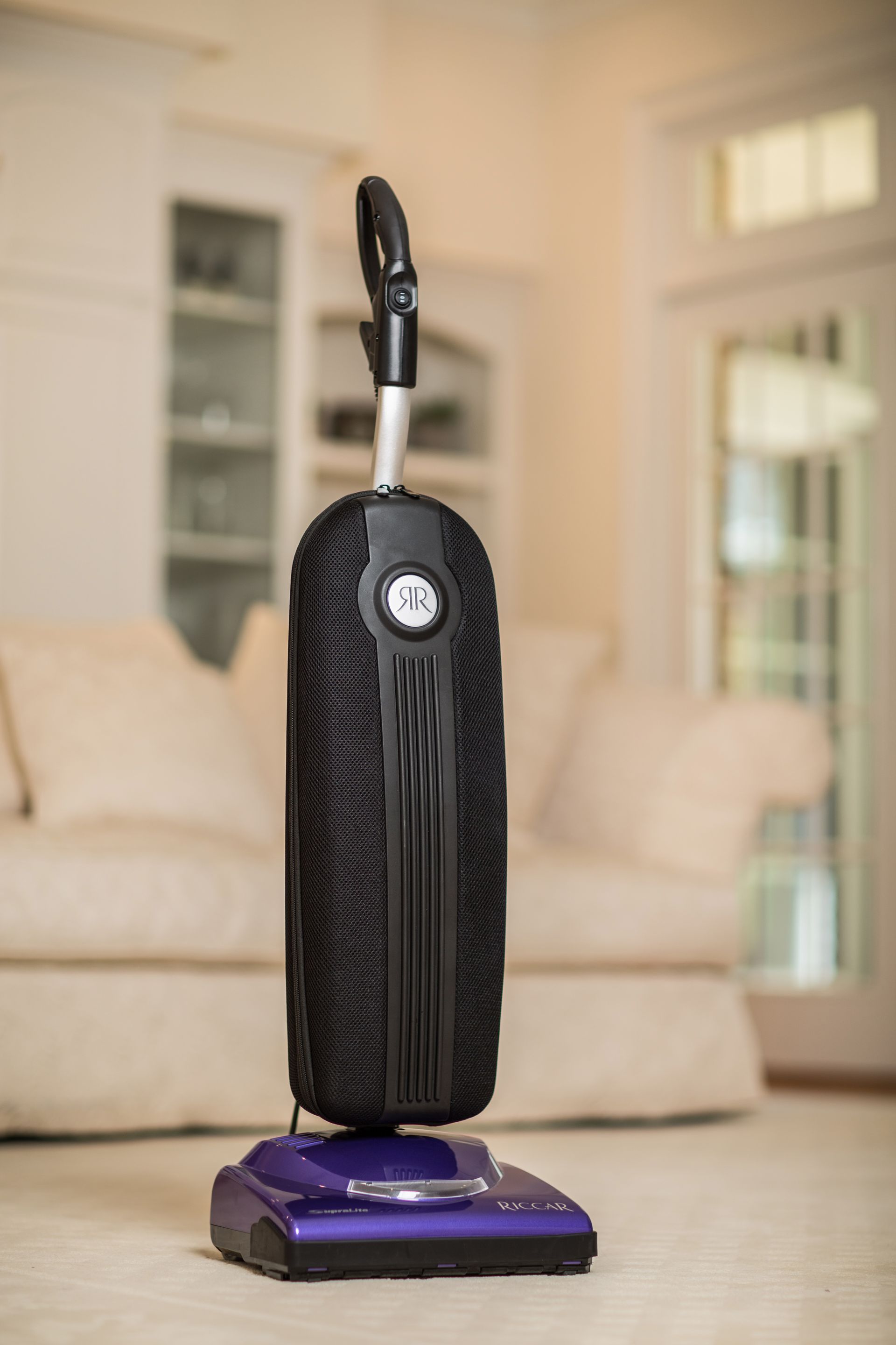 A purple vacuum cleaner is sitting on a carpet in a living room.