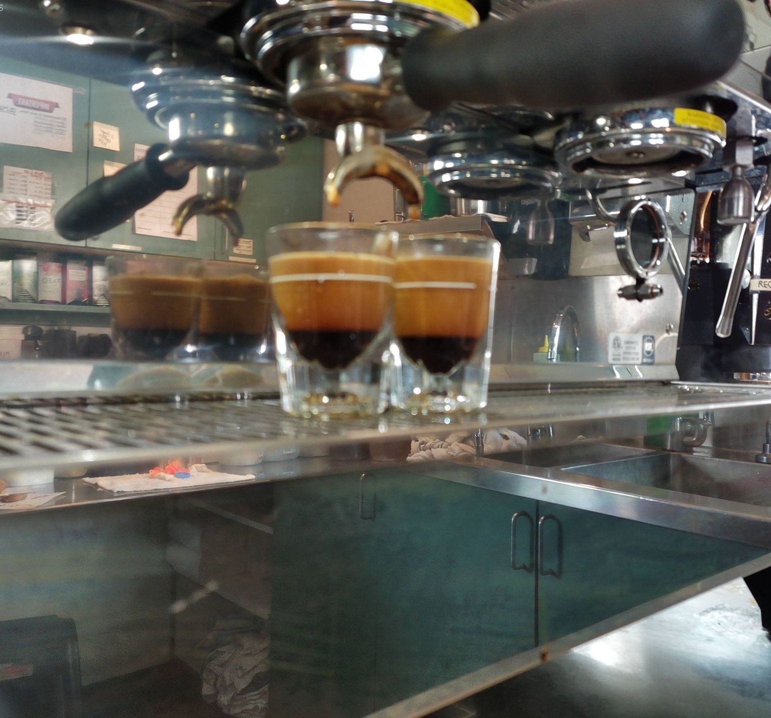 Two glasses of coffee are sitting on a counter in front of a coffee machine