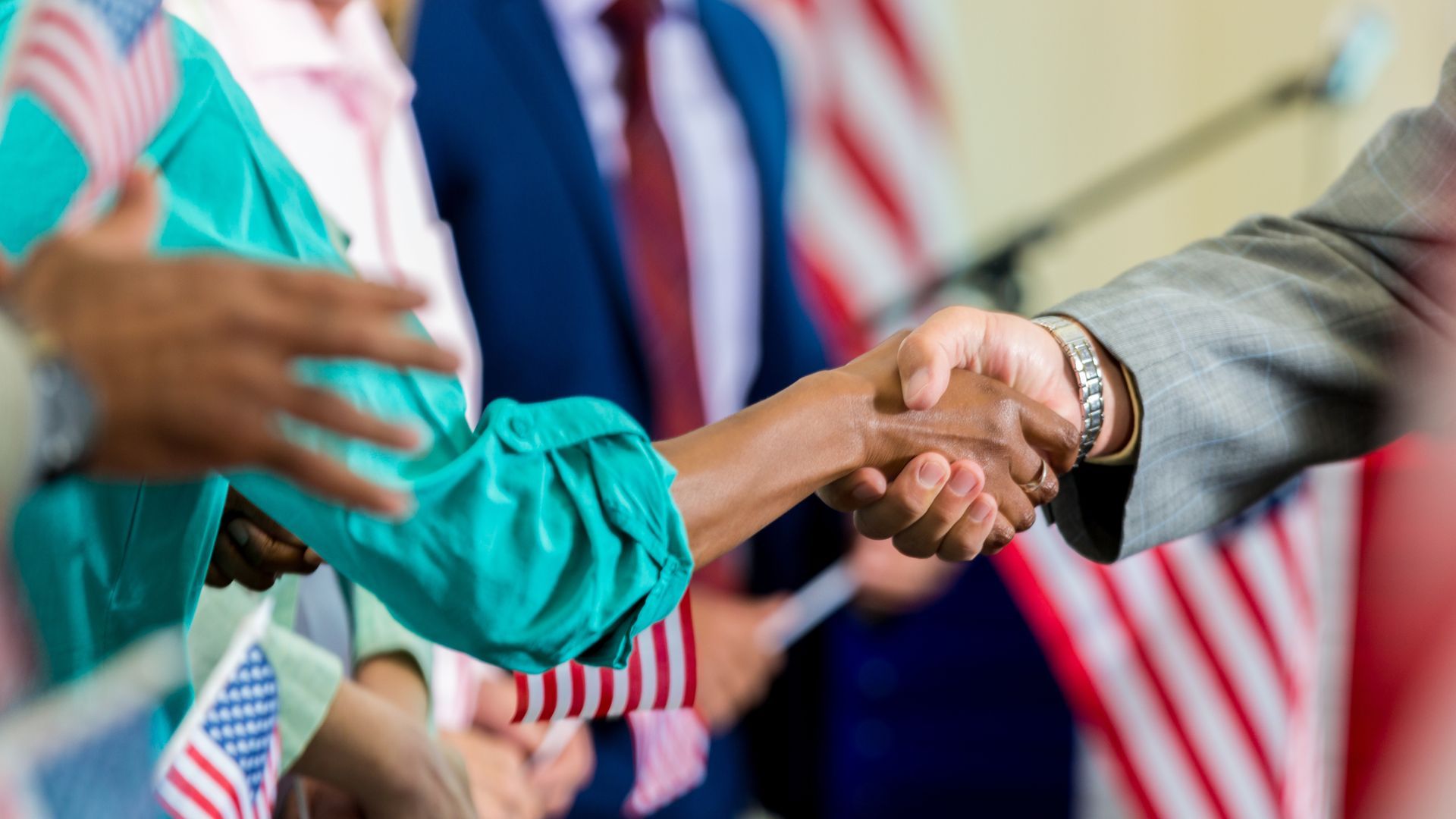 People shaking hands at an event with American flags in the background.