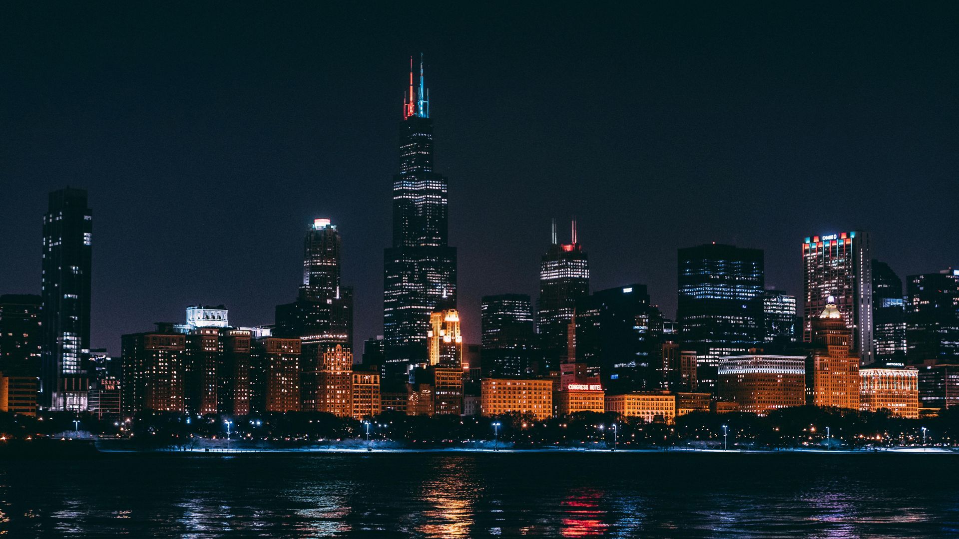 Nighttime Chicago skyline with illuminated skyscrapers reflected on water.
