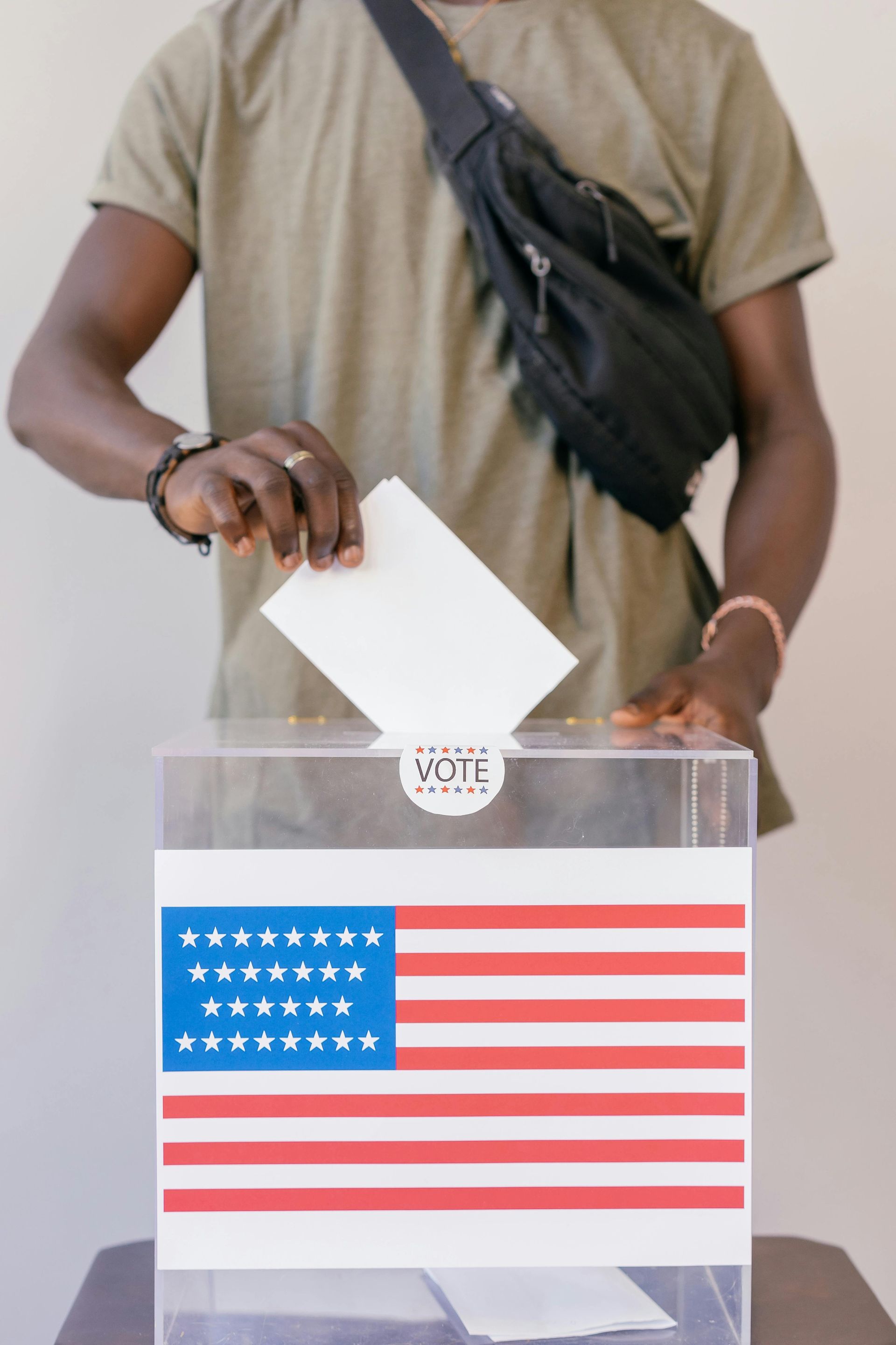 Person casting a ballot into a clear voting box displaying the American flag.