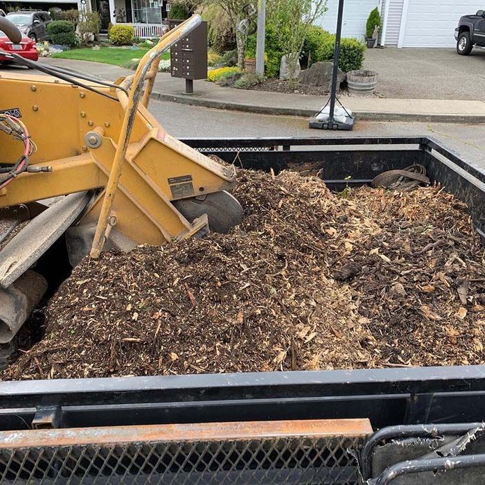 A large pile of mulch is being loaded into a trailer.
