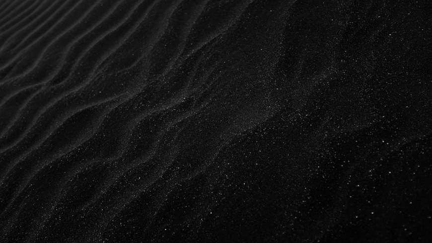 Black sand rippled into waves, speckled with faint sparkles.