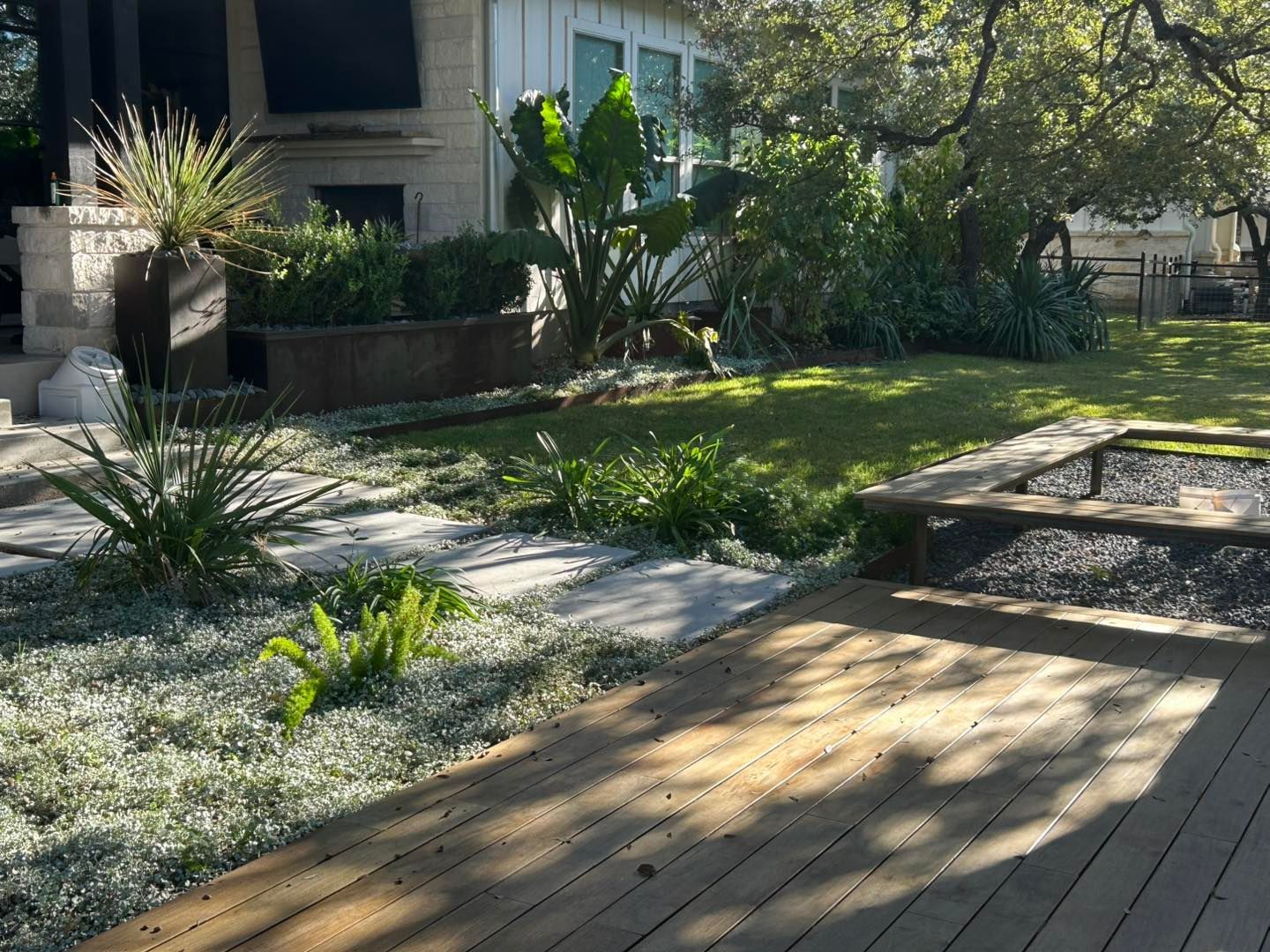Backyard with a wooden deck, green grass, plants, and a white house.