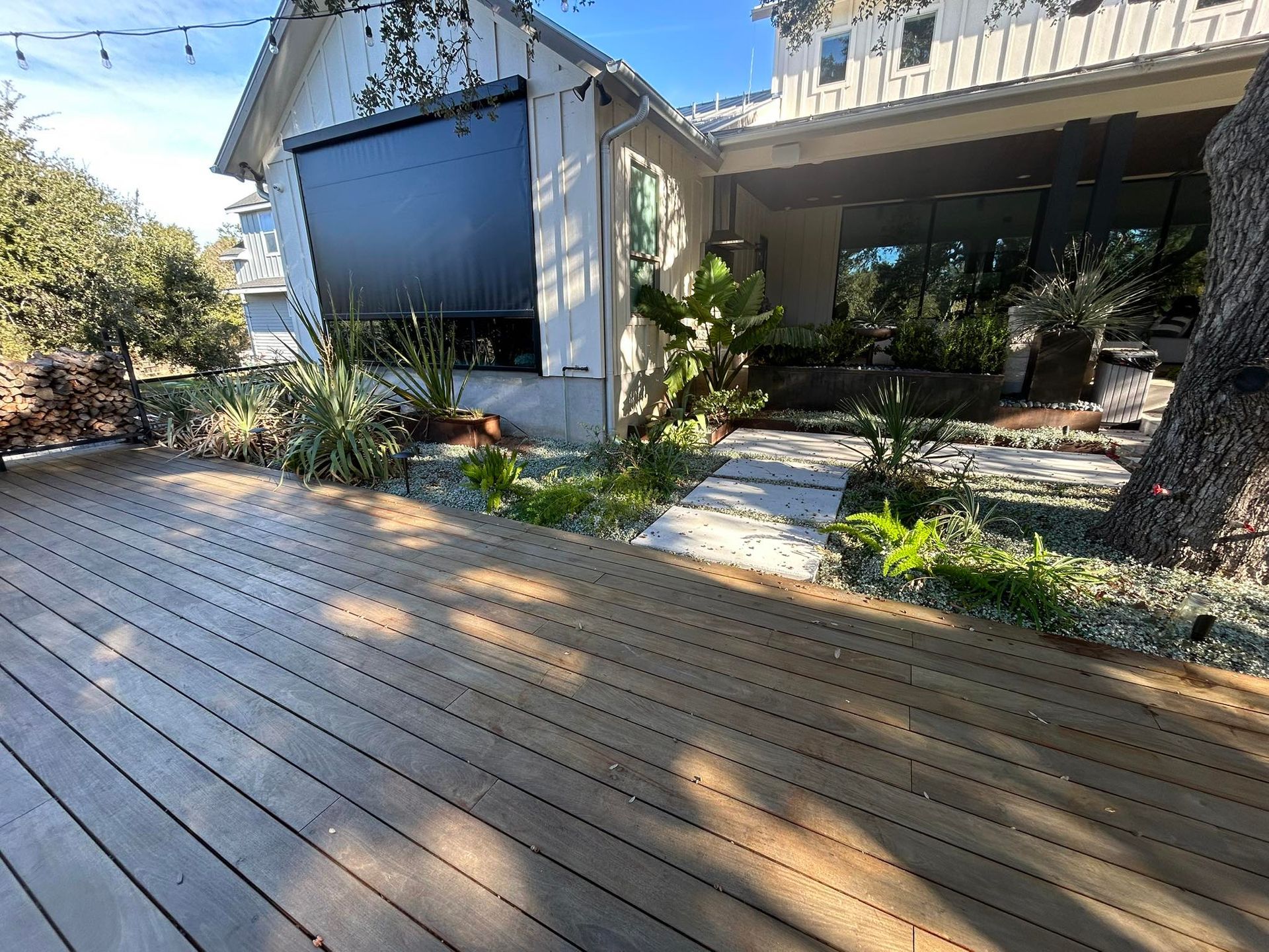 Wooden deck leads to a white house with a sun shade, landscaping, and a stone path.