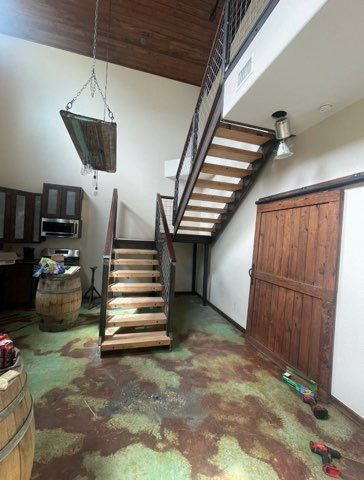 Two-story interior with stairs, wooden door, and a rustic aesthetic. Green and brown floor, light walls.