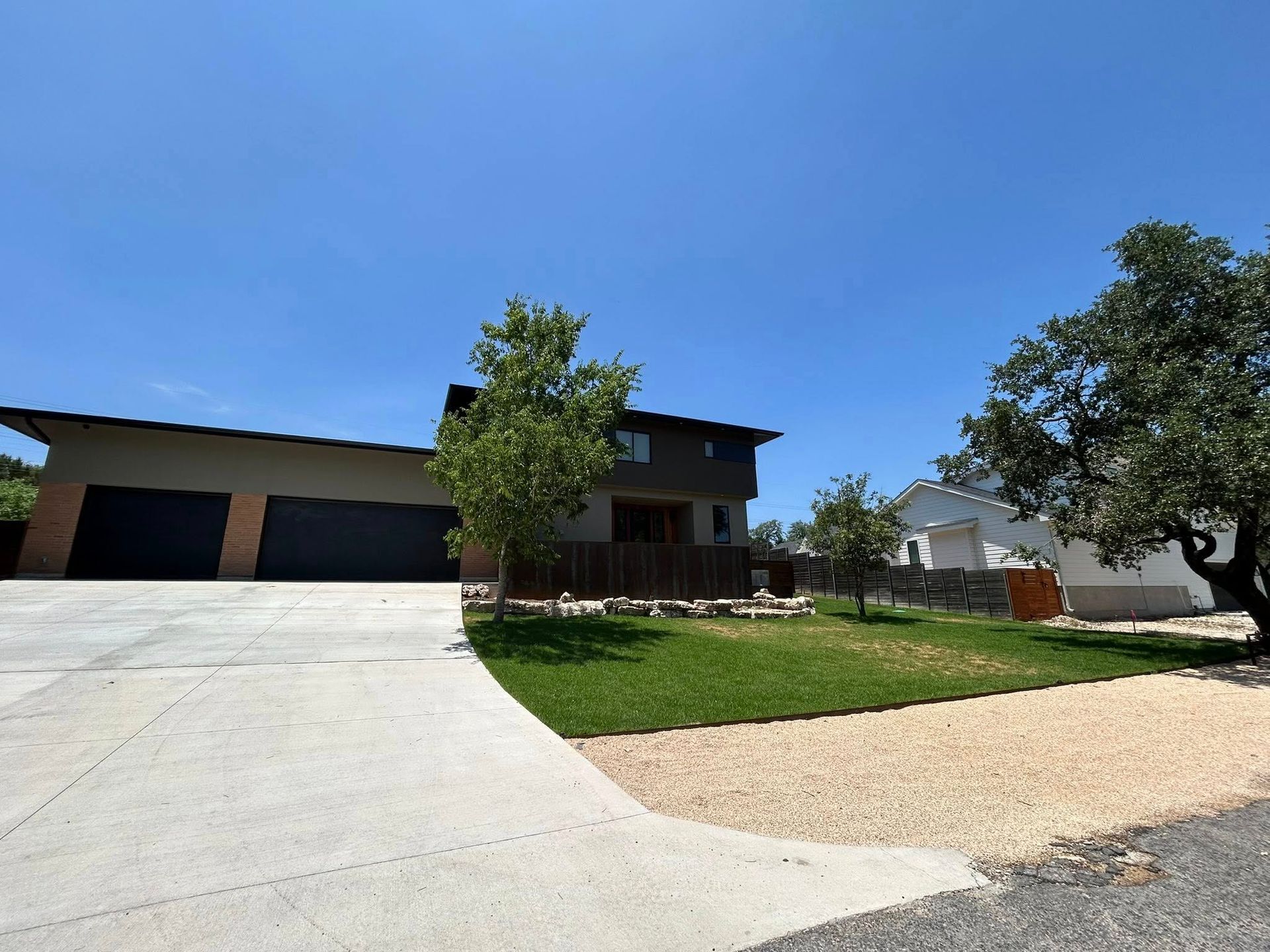 Modern two-story house with attached garage, driveway, and landscaping under a blue sky.