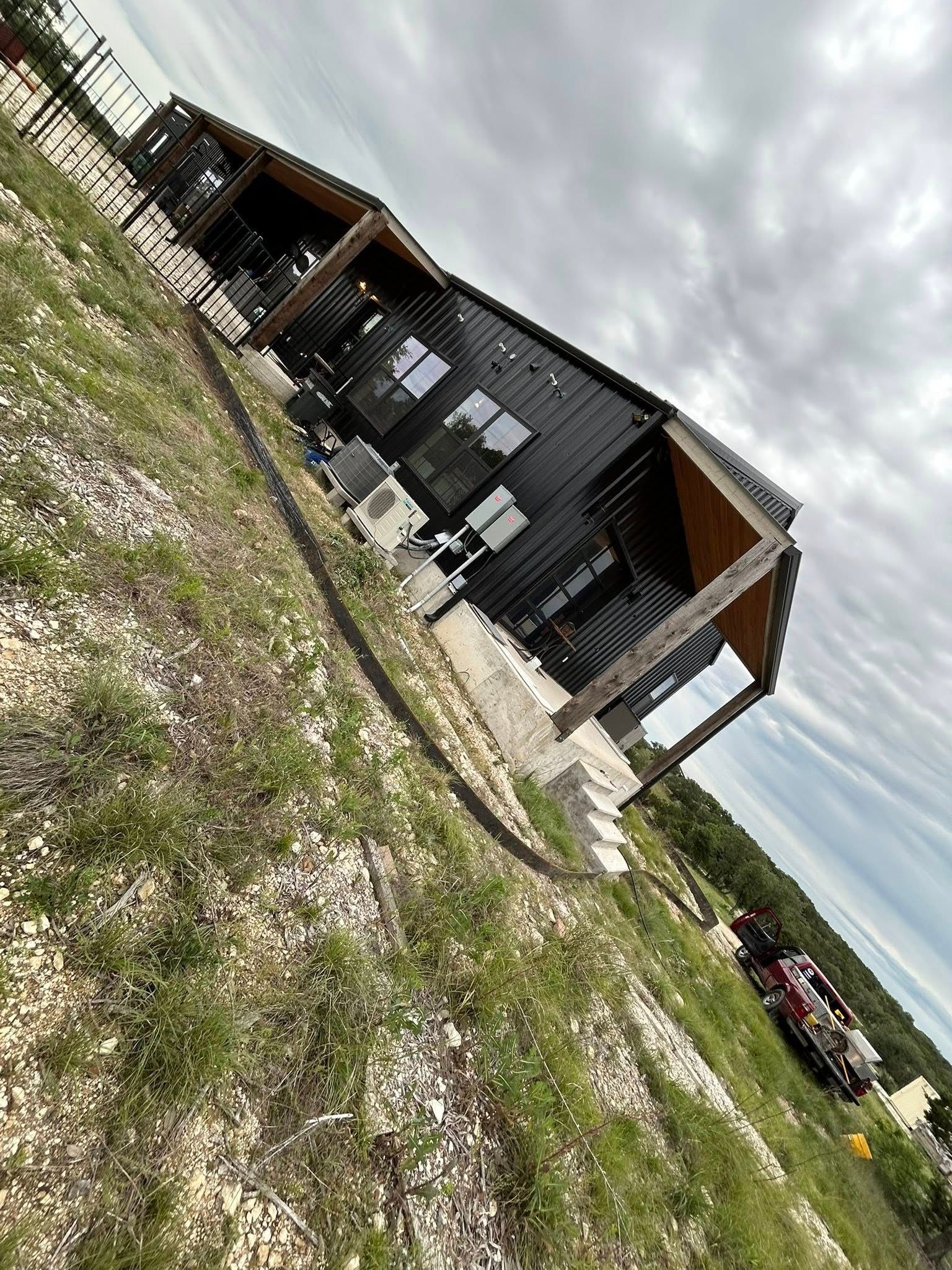 Black modern house on a hillside with a cloudy sky; porch with wooden beams.