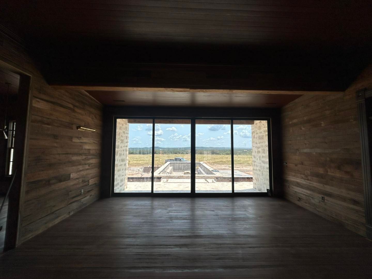 Empty room with wood panel walls, large glass door, and outdoor view of a field.