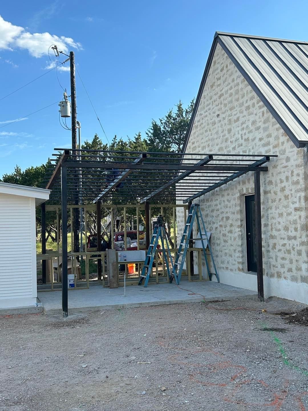 Construction of a black metal pergola attached to a stone building; workers on ladders.