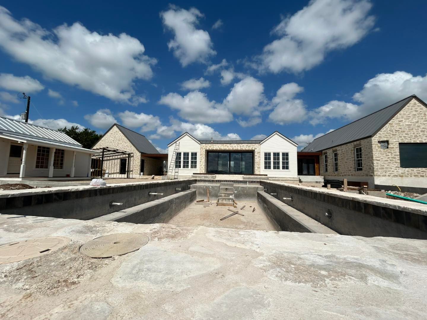 Construction site with empty pool, connected to house under construction, blue sky.