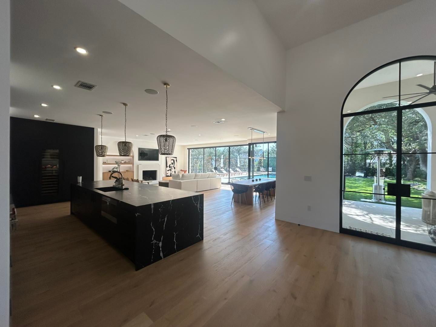 Spacious kitchen with black island, light wood floors, large arched windows overlooking a backyard.