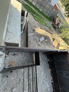 View of construction site with debris, dirt, metal structures, and a building, outdoors in daylight.