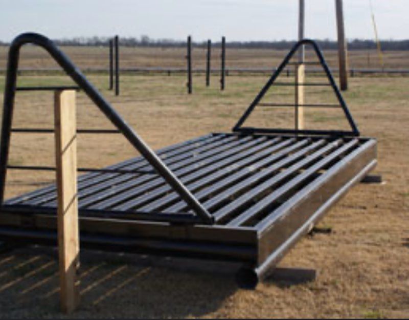 Black cattle guard on a grassy field, metal bars, with arched and triangular metal frames, wooden posts.
