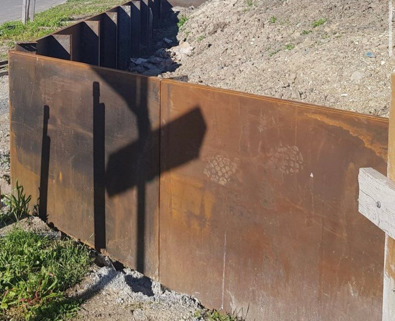 Rusty metal retaining wall curves along a slope, casting shadows.