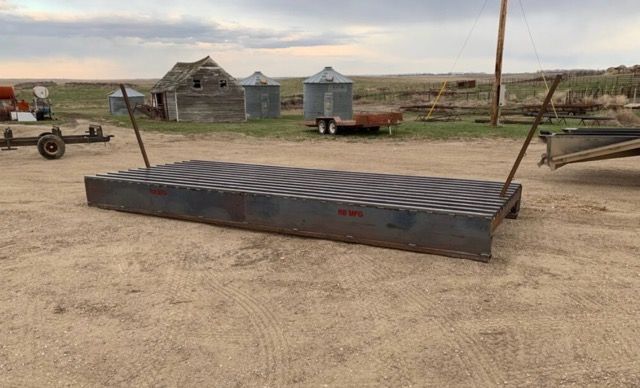 Metal cattle guard on a dirt road, with a rural backdrop of buildings and fields.