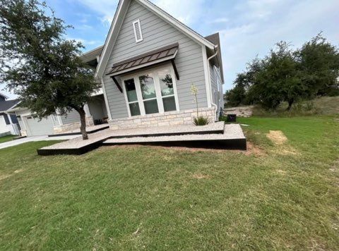 Gray house with stone facade, steps, and dark trim. Green lawn.