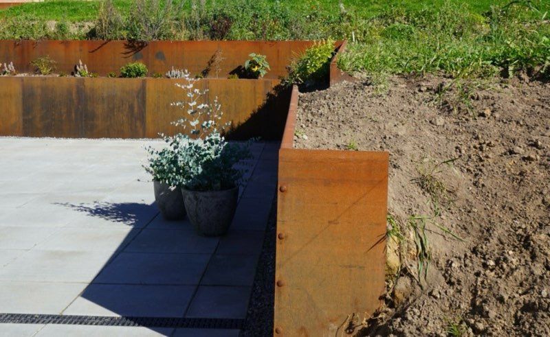 Rusty metal garden bed borders with plants and paved patio next to a grassy area.