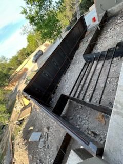 Construction site: metal forms for concrete wall; rebar rods extend from the base; gravel and dirt surround.