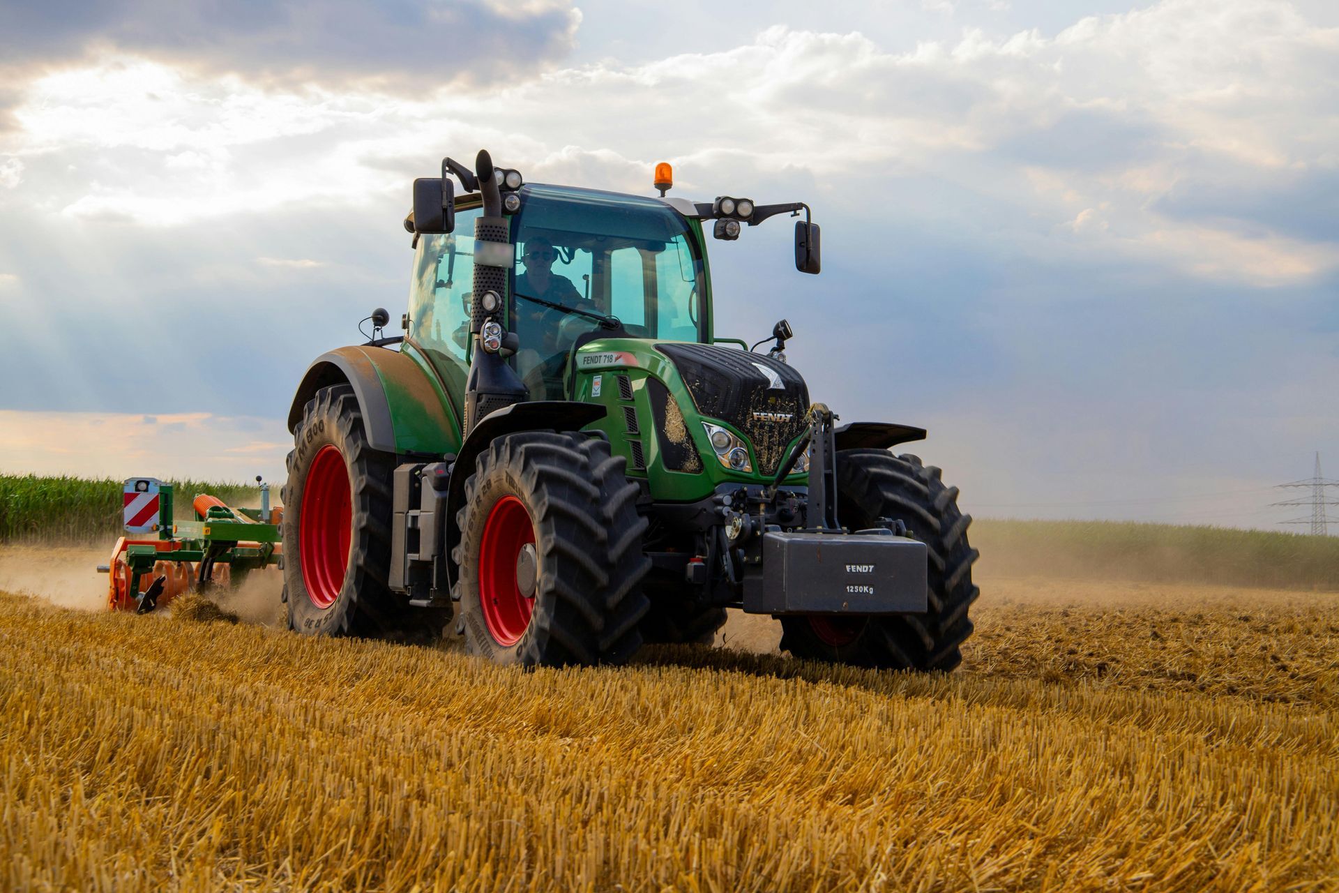 Green tractor plowing a field of wheat under a cloudy sky.