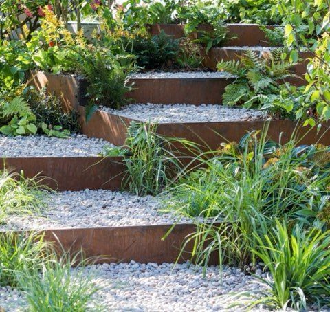 Rusty metal steps in a garden, filled with gravel and green plants.