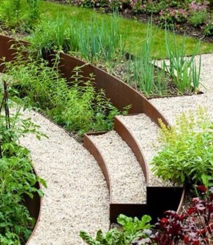 Tiered garden beds with curved metal borders, filled with various green plants and light gravel pathways.