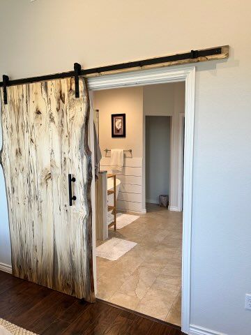 Rustic wooden barn door open to a bathroom with neutral decor and tile floors.
