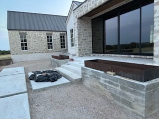 Exterior view of a modern home under construction with stone walls, concrete steps, and large windows.