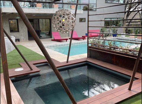 Outdoor pool area with a hot tub, pool, pink lounge chairs, and modern architecture.
