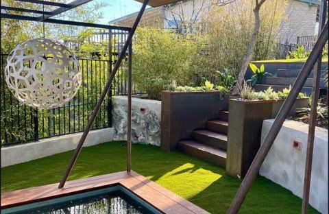 Backyard with artificial turf, decorative globe, small pool, stairs, and tiered landscaping.