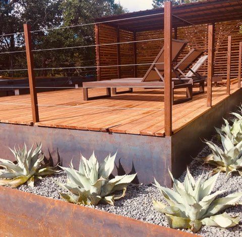 Wooden deck with lounge chairs, a metal planter with agave plants, and a natural backdrop.