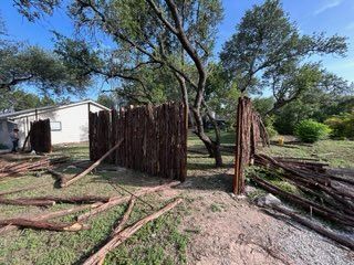 A rustic fence made of logs being constructed outdoors near a house.