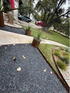 Black gravel path and grass area bordered with metal, trees, and vehicles in background.