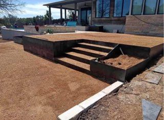 Outdoor patio with built-in steps, bordered by metal edging, on a gravel surface, near a house.